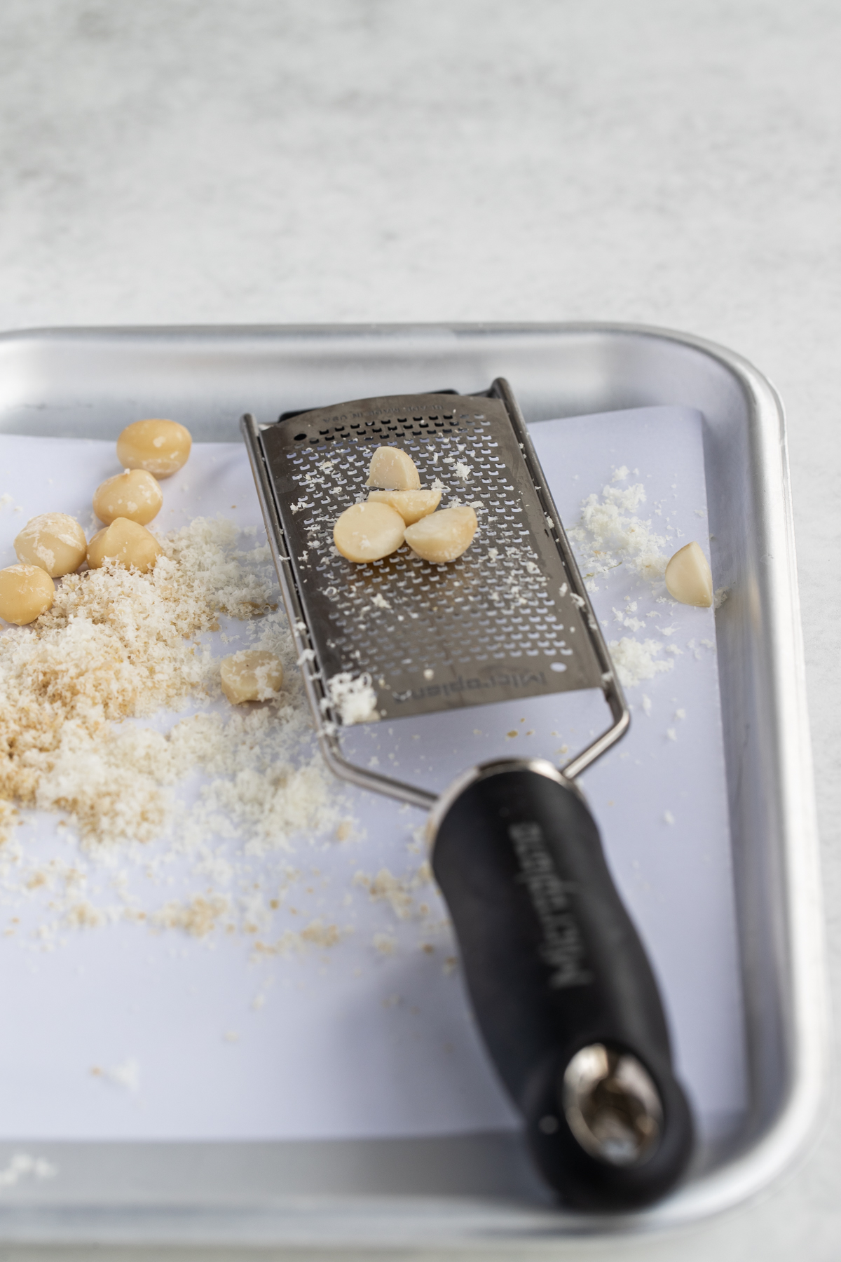 Microplane and grated macadamias on a silver tray and white background