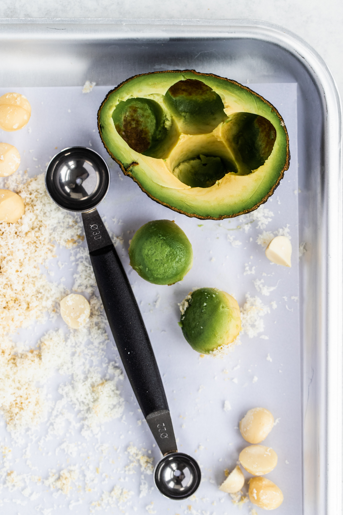 Melon baller and avocado balls with half and avocado and macadamias on a white background