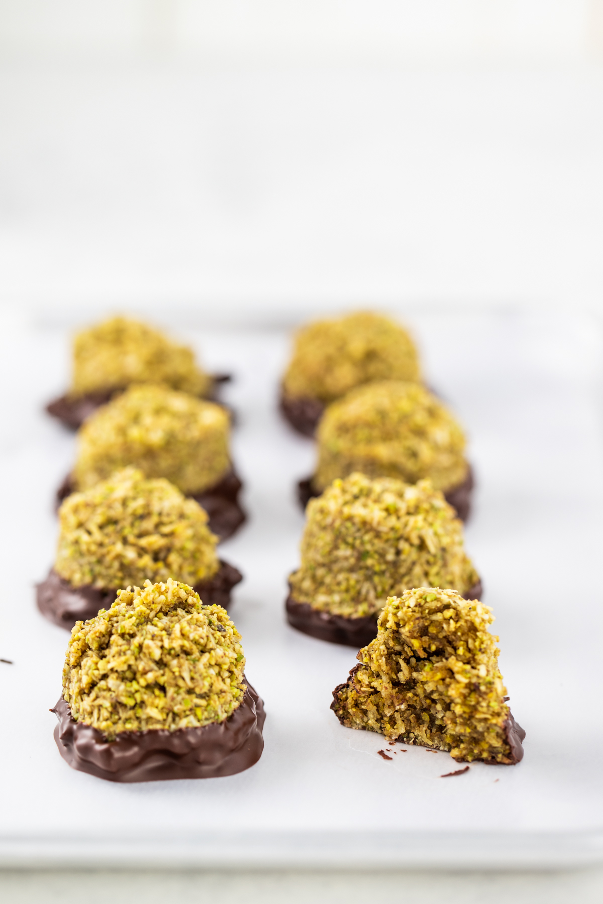 Chocolate dipped Pistachio Five Spice Macaroons on a white background.