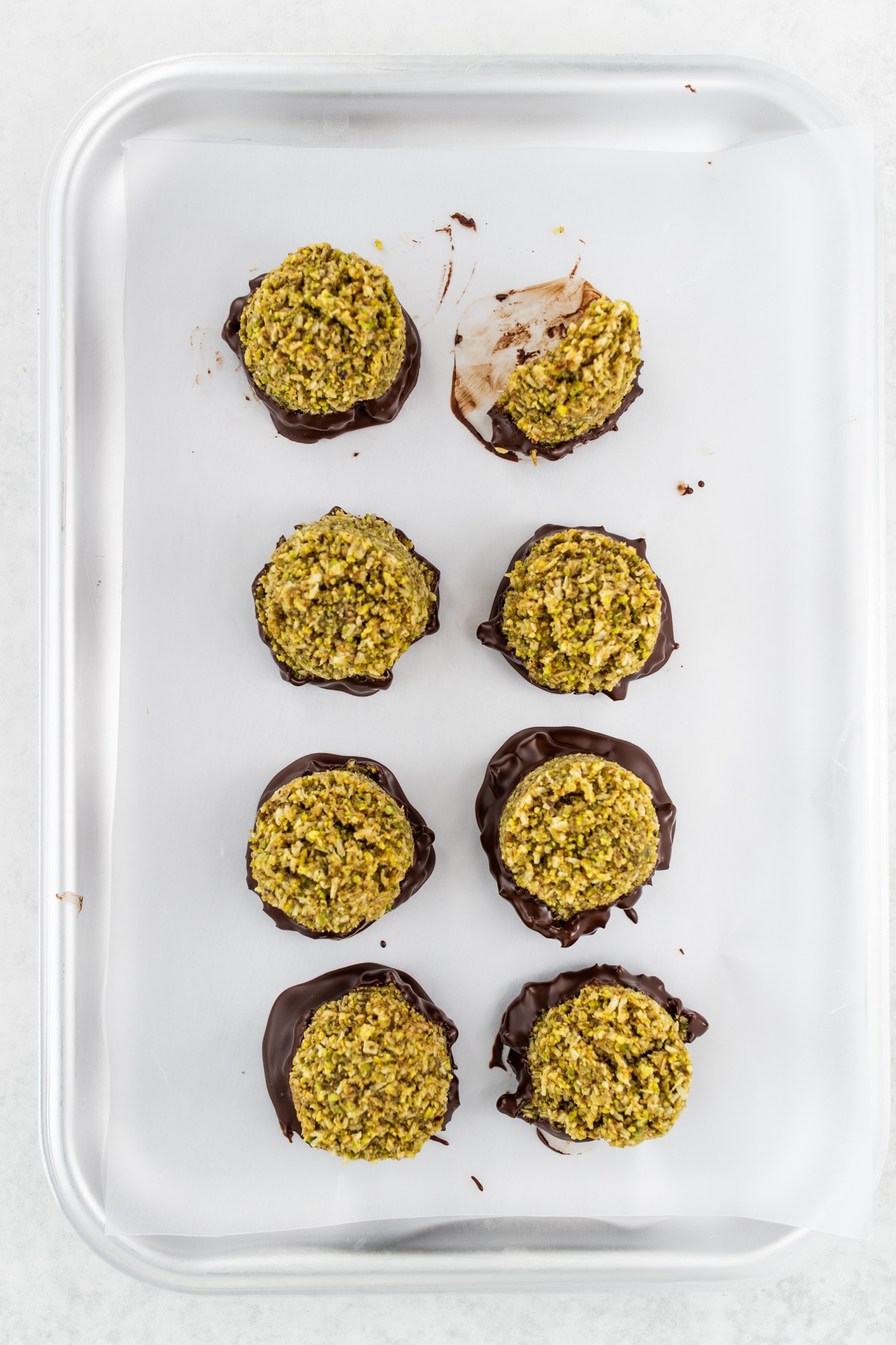 Overhead shot of Pistachio Five Spice Macaroons with chocolate dipped bases, on a white background.