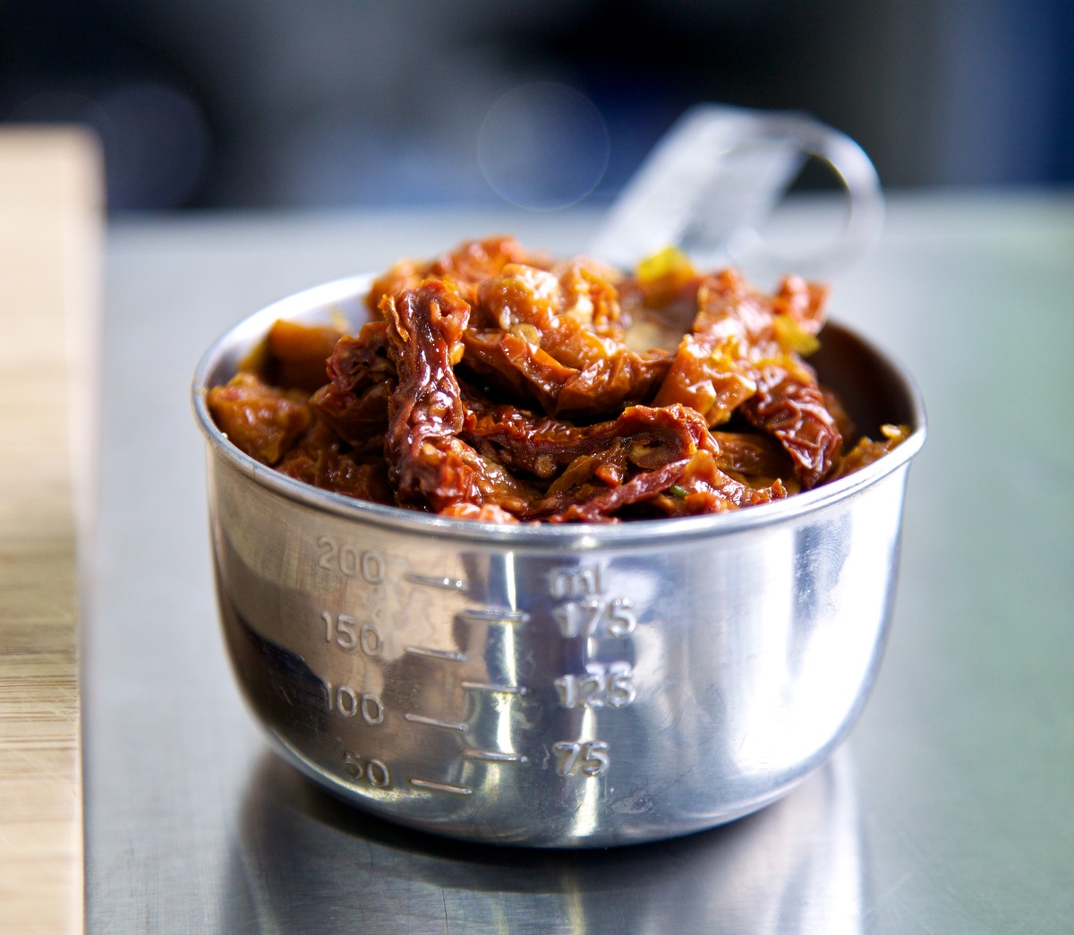 Soaked sundried tomatoes in a metal cup measure on a metal surface