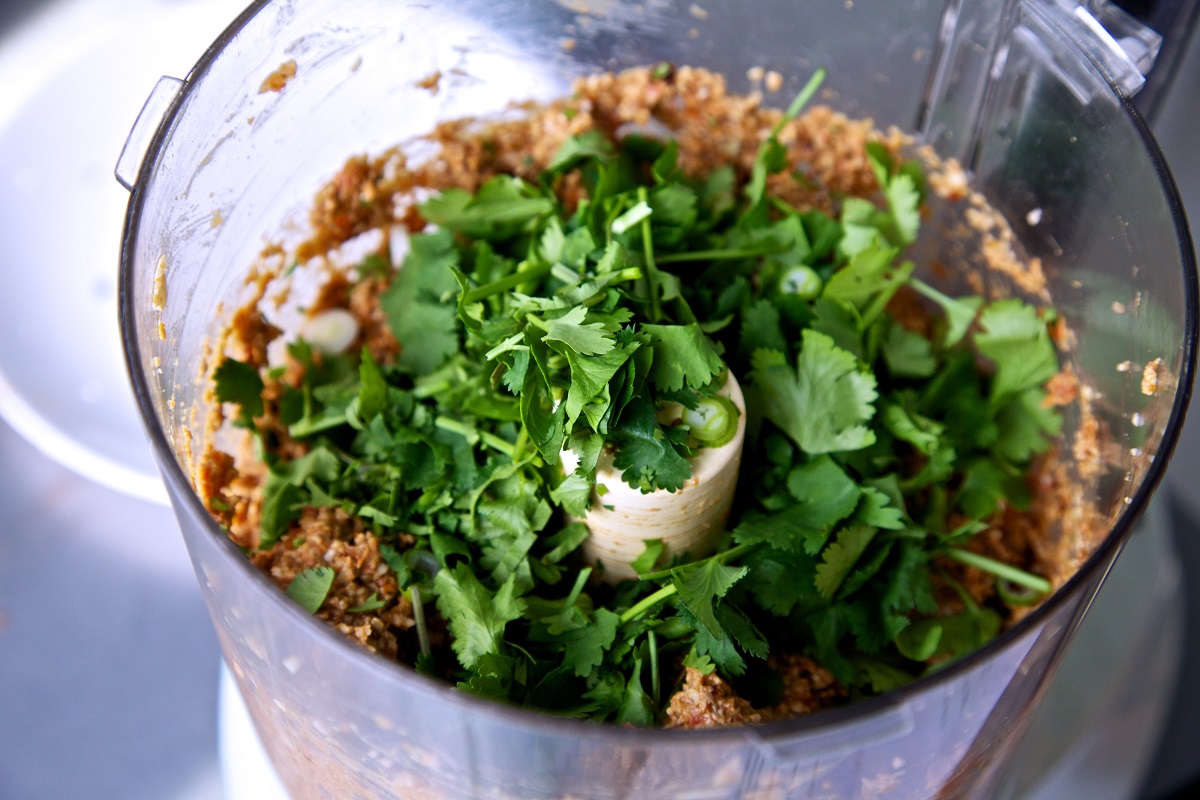 Cilantro on top of a smoky maple sunflower seed mixture in a food processor 