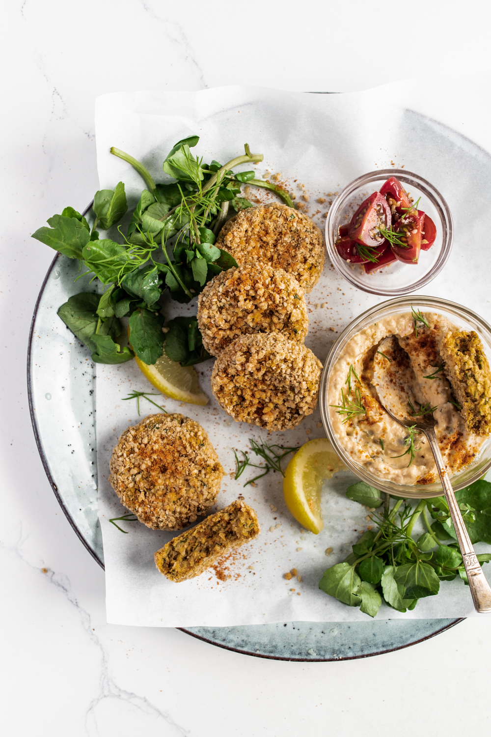 Fermented cauliflower crab cakes with horseradish dipping sauce with watercress on a white background